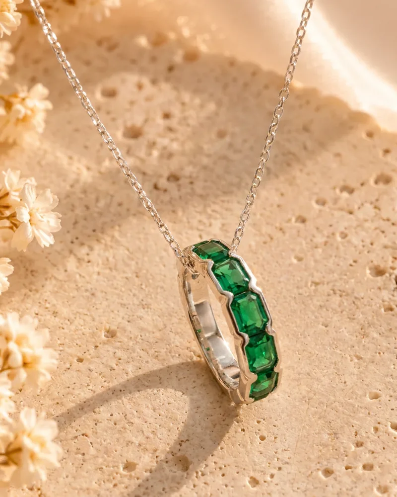 Anillo de plata con piedras verdes colgado de una cadena